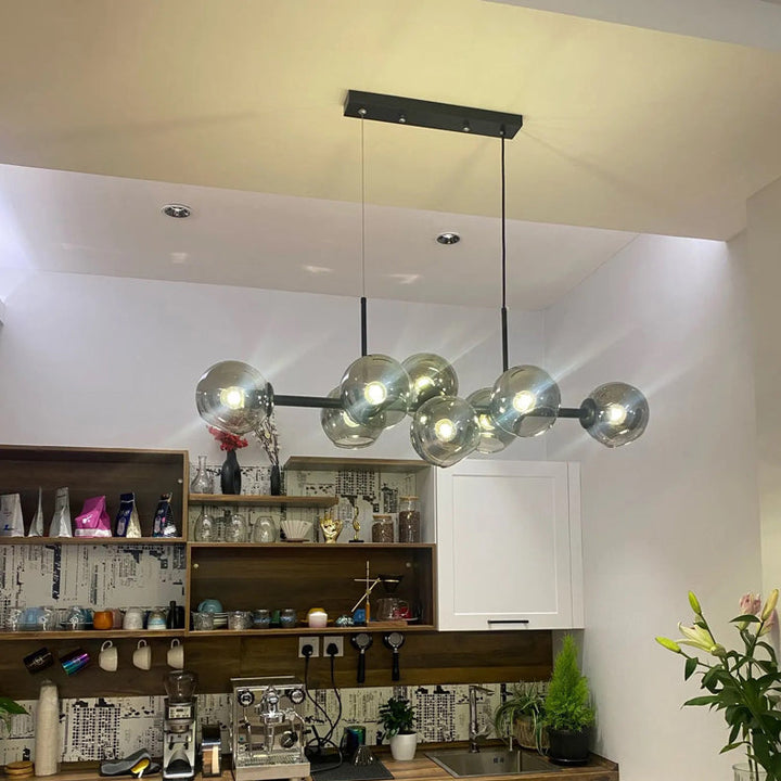 Suspension lumineuse haut de gamme en verre et métal noir installée au-dessus d'un espace bar.