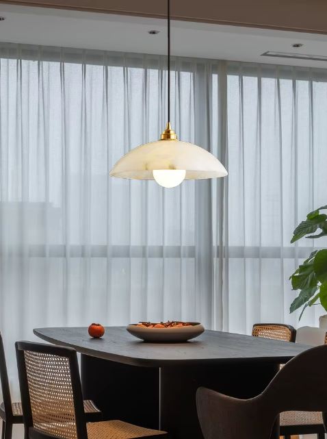 Suspension en marbre blanc avec finition dorée, illuminant une table à manger avec une ambiance raffinée et chaleureuse.