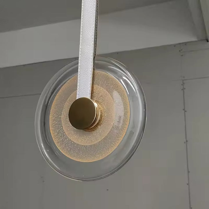 Suspension médaillon en verre avec lanière blanche en cuir et finition dorée, au design chic, épuré et contemporain