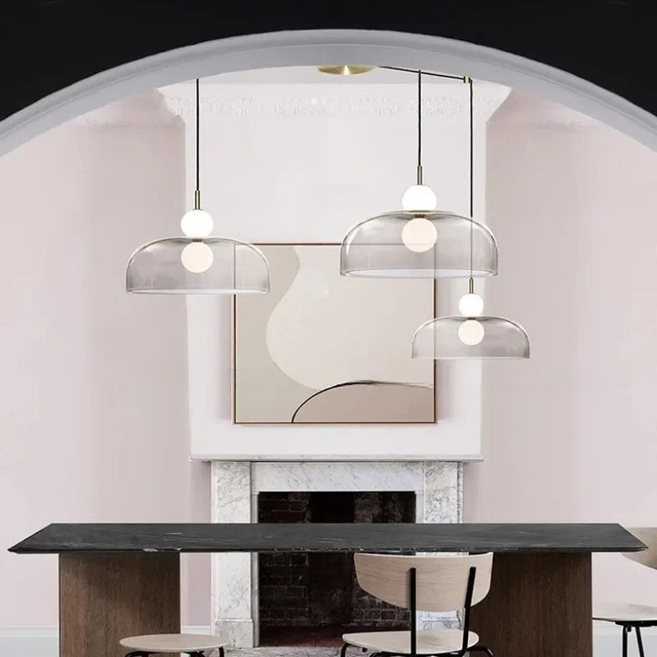 Trio de suspensions design transparentes légèrement fumées à doubles globes opalins suspendues au-dessus d'une table à manger.