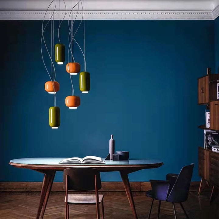 Ensemble de suspensions Monolithe Space Age multicolores disposées en hauteur devant un mur bleu profond.