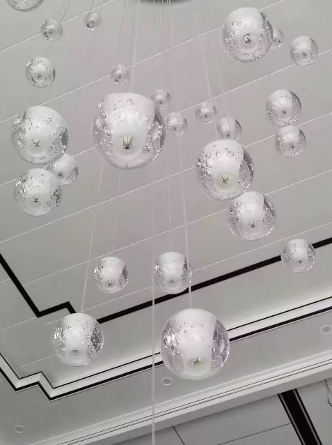 Suspension multiple de globes en verre bullé façon nuage lumineux, luminaire design moderne pour plafond haut.