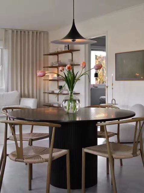 Suspension noire au-dessus d’une table ronde, mêlant lignes modernistes, sobriété scandinave et charme vintage.