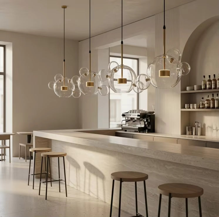 Quatre suspensions à bulles de verre soufflé transparent et détails dorés éclairent un comptoir de bar au style contemporain.