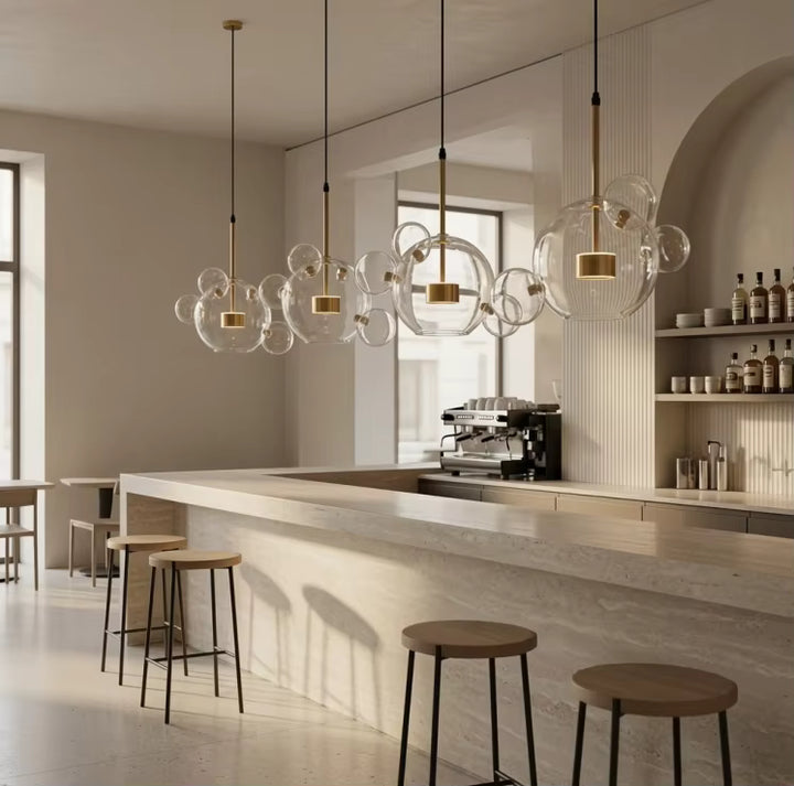 Quatre suspensions à bulles de verre soufflé transparent et détails dorés éclairent un comptoir de bar au style contemporain.