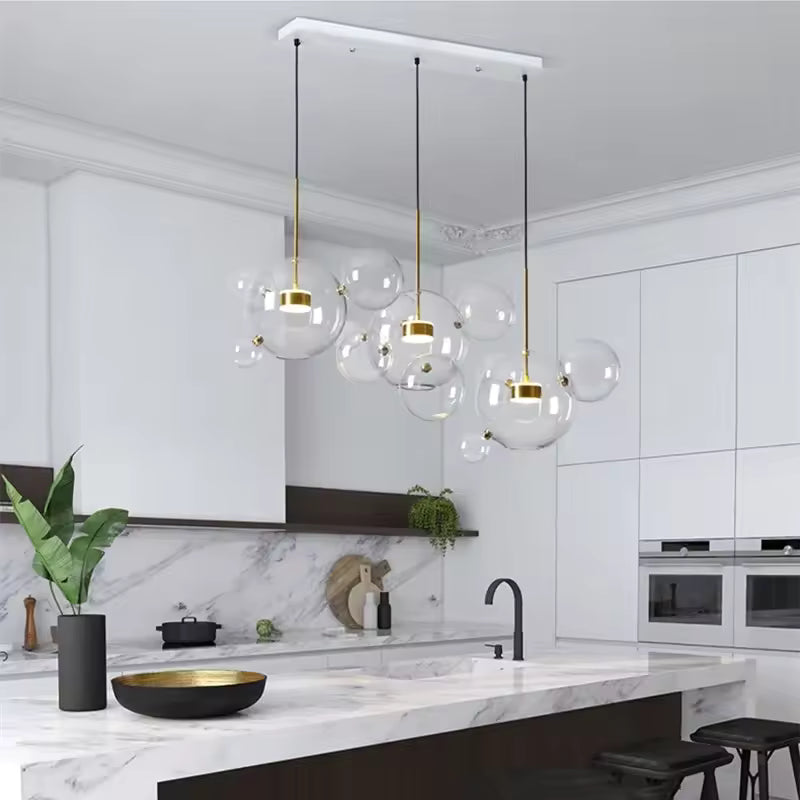 Au-dessus d'un îlot de cuisine en marbre, trois suspensions à bulles de verre soufflé allient design aérien et élégance moderne.