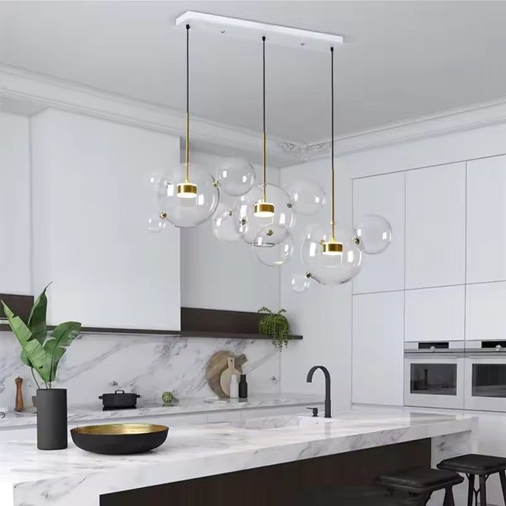 Au-dessus d'un îlot de cuisine en marbre, trois suspensions à bulles de verre soufflé allient design aérien et élégance moderne.
