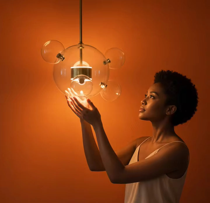 Face à un fond orangé, une suspension nuage de bulles en verre soufflé transparent diffuse une lumière chaude et douce.