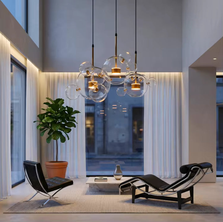 Trois suspensions nuage de bulles en verre soufflé transparent illuminent un salon design à haut plafond.