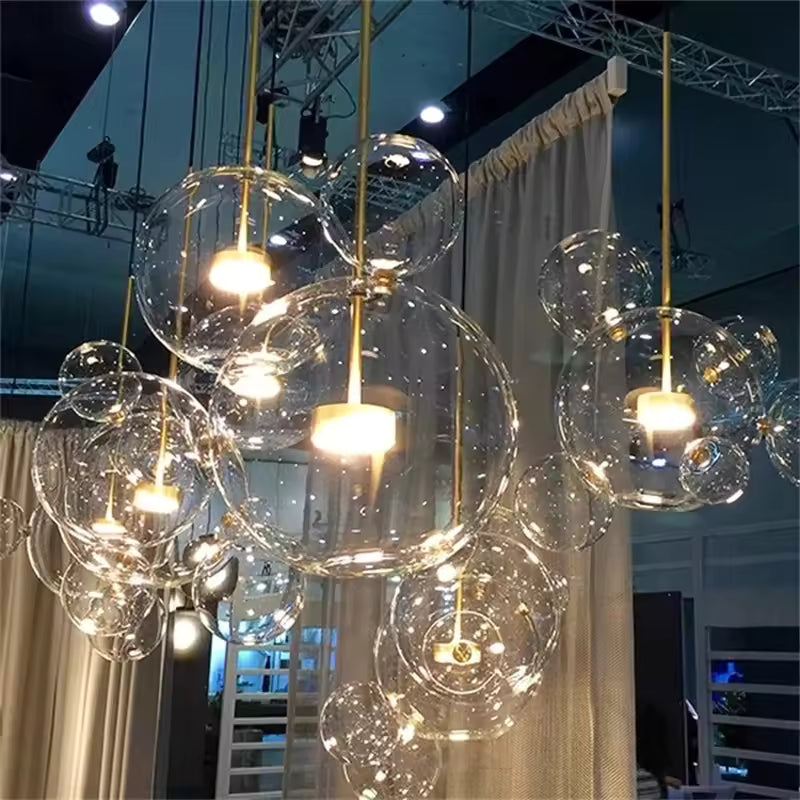 Vue rapprochée de suspensions à bulles en verre soufflé transparent, illuminées par des LED dorées au design sculptural.
