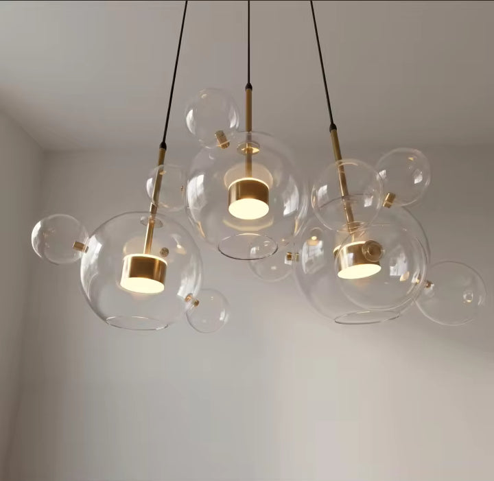 Vue en contre-plongée de trois suspensions à bulles en verre soufflé transparent, aux LED dorées et au style contemporain.