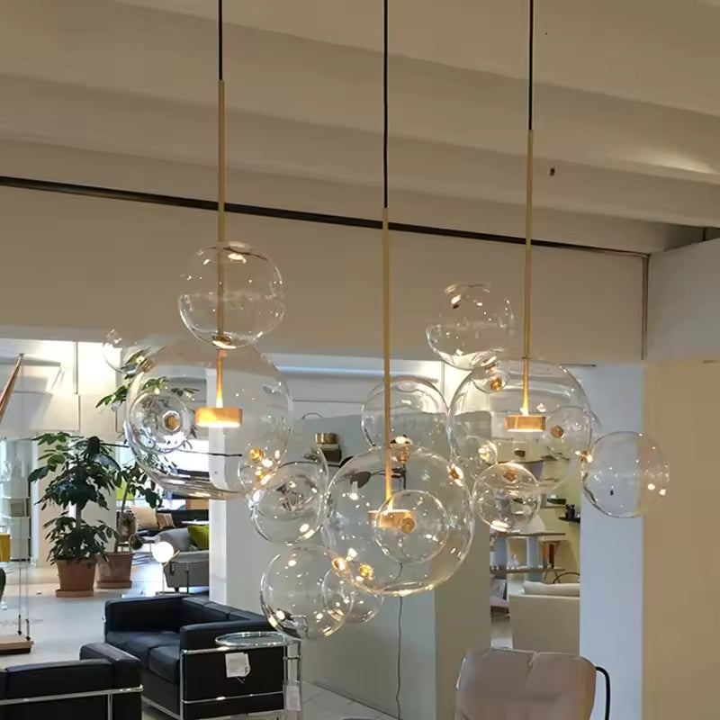 Trois suspensions dorées aux bulles de verre soufflé transparent, formant un nuage aérien dans un salon contemporain.