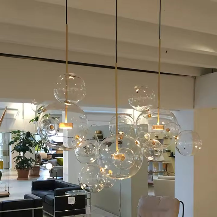 Trois suspensions dorées aux bulles de verre soufflé transparent, formant un nuage aérien dans un salon contemporain.