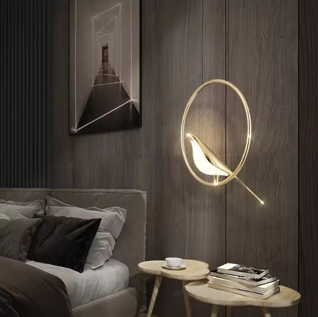 Suspension murale dorée en forme d’oiseau perché dans un anneau lumineux, idéale en lampe d’ambiance chic pour une chambre moderne.