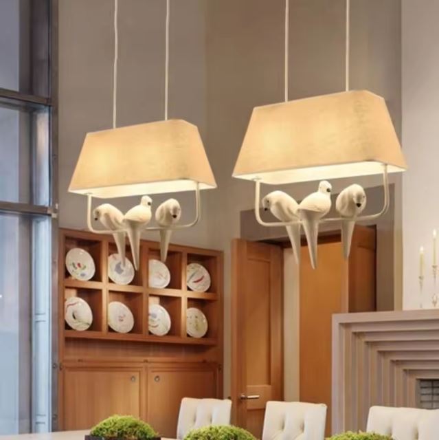 Double suspension luminaire avec oiseaux sur branche, idéale pour une salle à manger au design chaleureux et moderne.