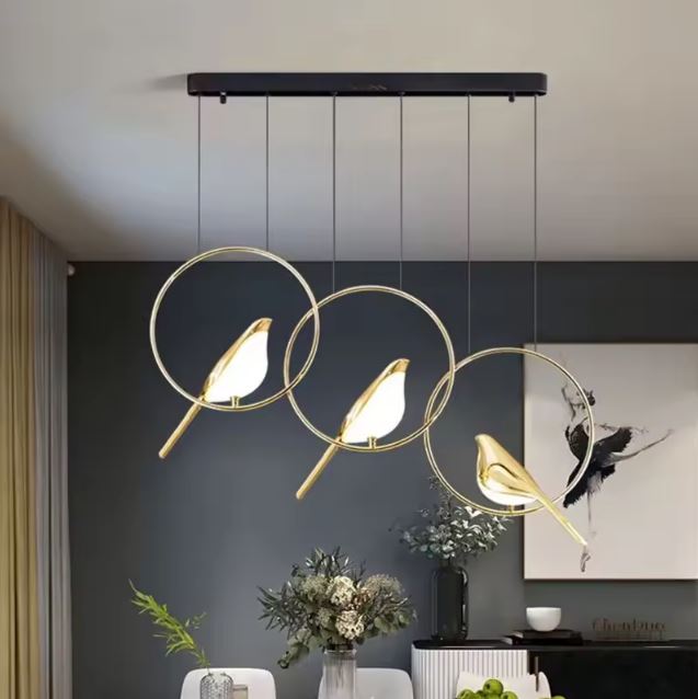 Suspension design à trois oiseaux lumineux dorés dans des anneaux fins, idéale pour une salle à manger poétique et au style contemporain.