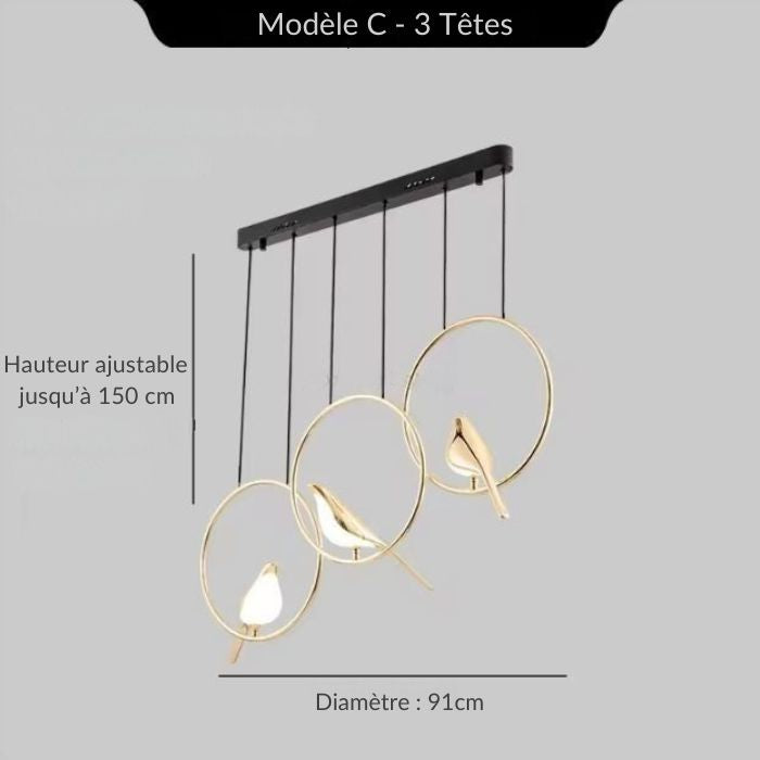 Suspension design avec 3 oiseaux dorés dans des anneaux lumineux dorés, longueur 91 cm, idéale au-dessus d’un îlot ou d’une table moderne.