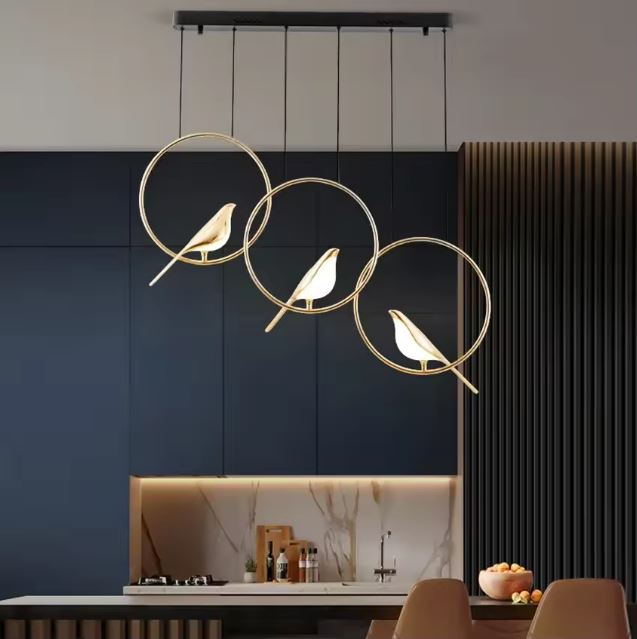 Suspension moderne à trois oiseaux lumineux dorés dans des cercles suspendus, idéale pour une cuisine au design épuré et élégant.