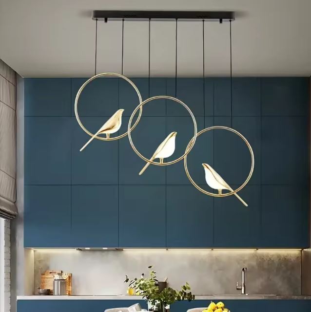 Suspension moderne à trois oiseaux lumineux cerclés de doré, idéale pour cuisine design ou coin repas à l’esthétique poétique et chic.