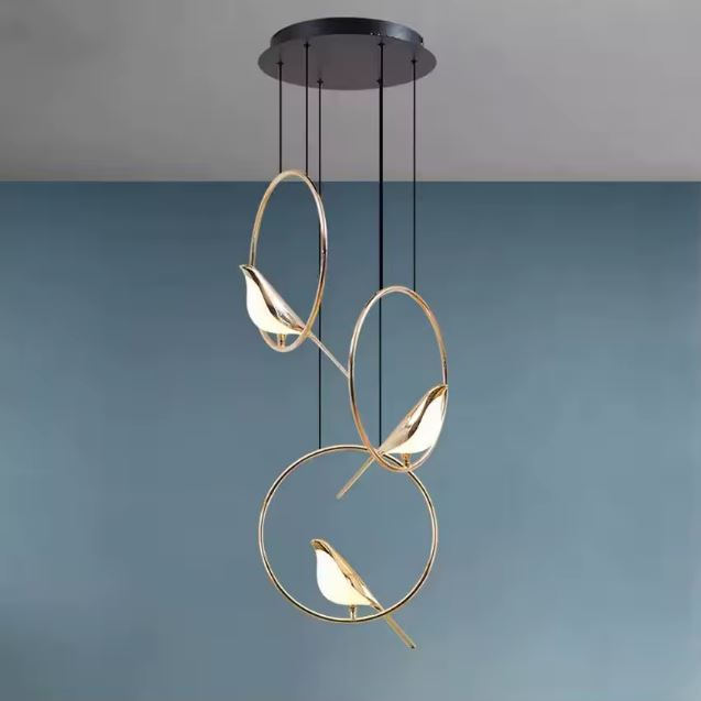 Suspension design verticale à trois oiseaux lumineux dorés dans des anneaux, parfaite pour une grande hauteur sous plafond moderne.