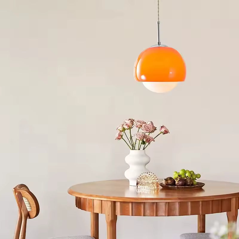 Au-dessus d’une table en bois, suspension orange à globe opalin au style rétro et aux lignes arrondies