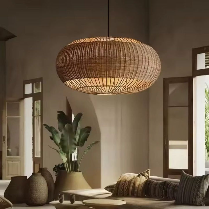 Dans un salon chaleureux, grande suspension ovale en rotin tressé ajouré, au design naturel et méditerranéen.
