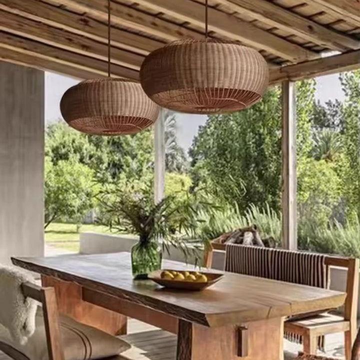 Deux suspensions ovales en rotin tressé surplombent une table en bois sous une terrasse couverte au style méditerranéen.