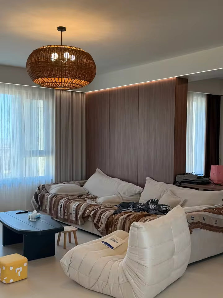 Dans un salon contemporain, grande suspension ovale en rotin tressé brun, au design bohème chic et à la lumière chaleureuse.