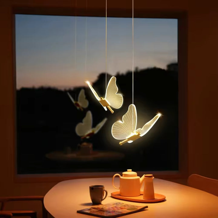 Deux papillons lumineux aux ailes transparentes composent un luminaire poétique et aérien au-dessus de la table