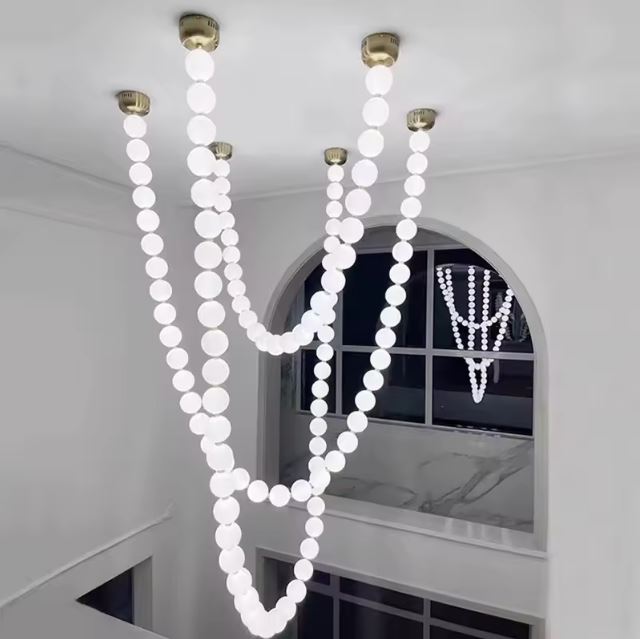 Suspension perle luxueuse illuminant un escalier avec un plafond haut et une fenêtre arquée pour un design raffiné.