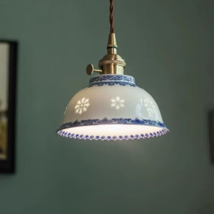 Suspension en porcelaine fine aux arabesques bleues ajourées, éclairée, évoquant un style vintage doux mêlé à une ambiance campagne chic.