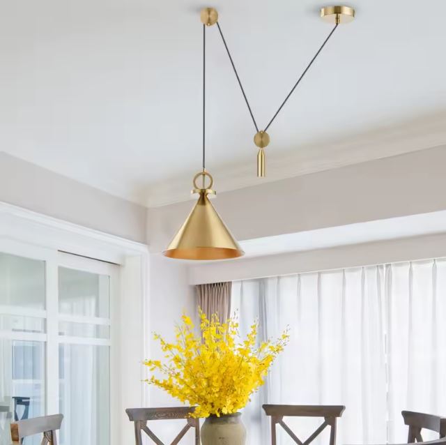 Suspension à poulie en laiton doré installée au-dessus d'une table de salle à manger lumineuse.