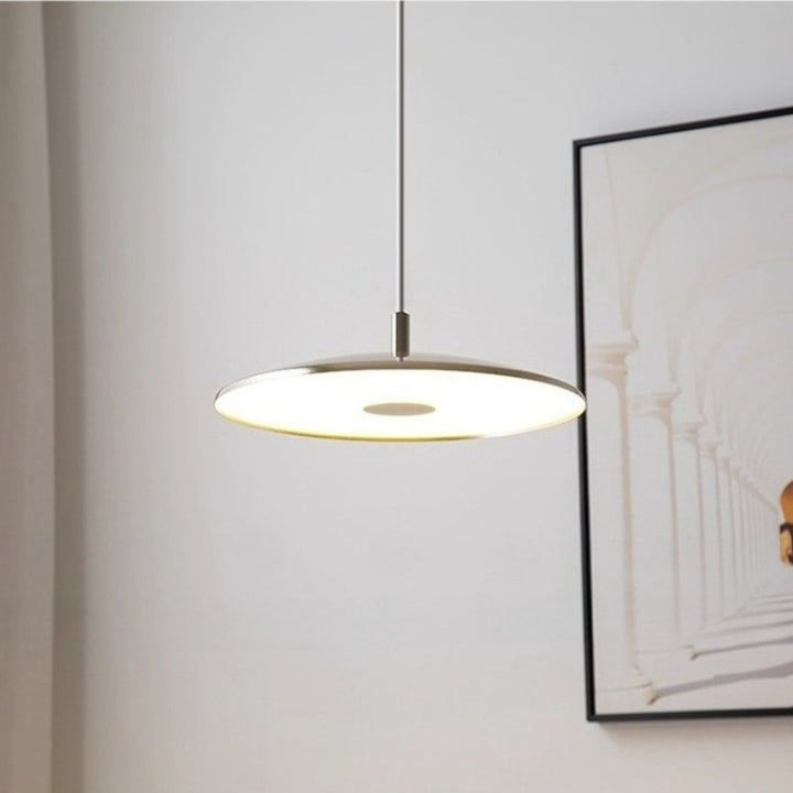 Vue rapprochée d'une suspension design ronde en métal diffusant une lumière chaleureuse dans un salon.