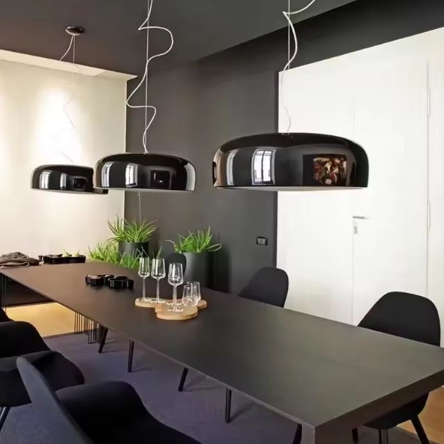 Trio de suspensions rondes noires design au-dessus d'une grande table, parfaites pour une salle de réunion moderne et élégante.
