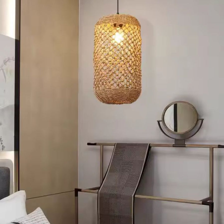 Suspension cylindrique en rotin à mailles ajourées, diffusant une lumière chaude près d'un miroir, dans un décor japandi.