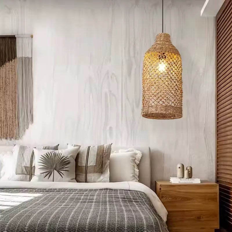 Près d'un lit, suspension cylindrique en rotin à mailles ajourées diffusant une lumière chaleureuse, au style bohème naturel.