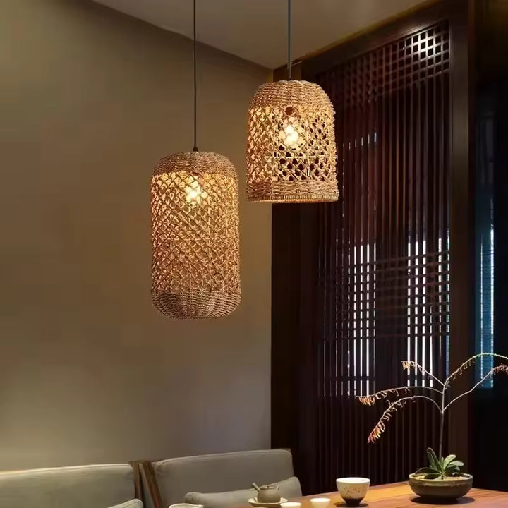 Deux suspensions cylindriques en rotin tressé ajouré diffusent une lumière chaude au-dessus d'une table à thé, dans un décor zen.