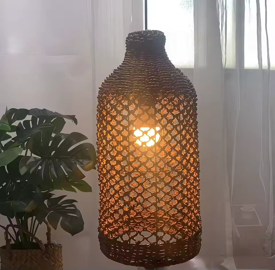 Gros plan sur une suspension en rotin tressé à mailles ajourées, de forme bouteille, diffusant une lumière chaude et douce.