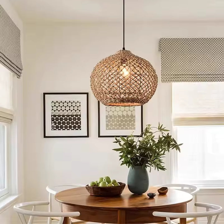 Au-dessus d'une table ronde en bois, suspension en rotin tressé à mailles ajourées, au style scandinave et naturel.