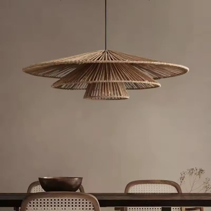 Au-dessus d'une table en bois, suspension en rotin à trois abat-jour coniques étagés, au style japandi et naturel.