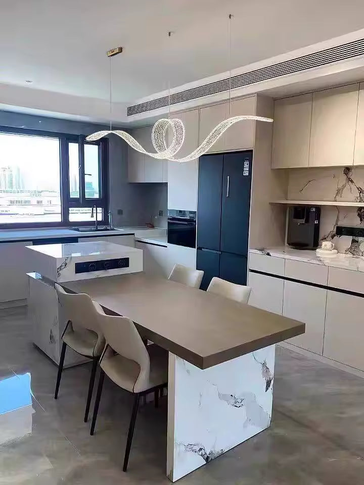 Au-dessus d'un îlot de cuisine, suspension LED design en ruban ondulé avec boucle centrale, au style contemporain sculptural.