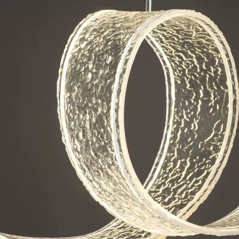 Gros plan sur la boucle centrale texturée d'une suspension LED en ruban ondulé, au design sculptural et contemporain.