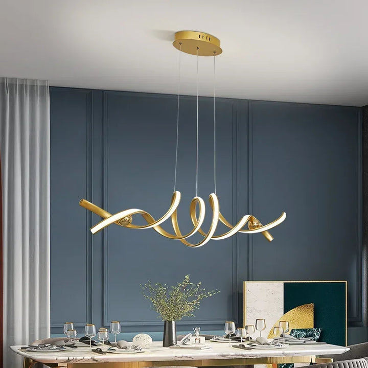 Suspension LED dorée à ruban torsadé design au-dessus d'une table de salle à manger élégante.
