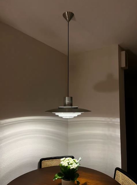 Suspension scandinave vintage à disques chromés, diffusant une lumière graphique au-dessus d'une table à manger.
