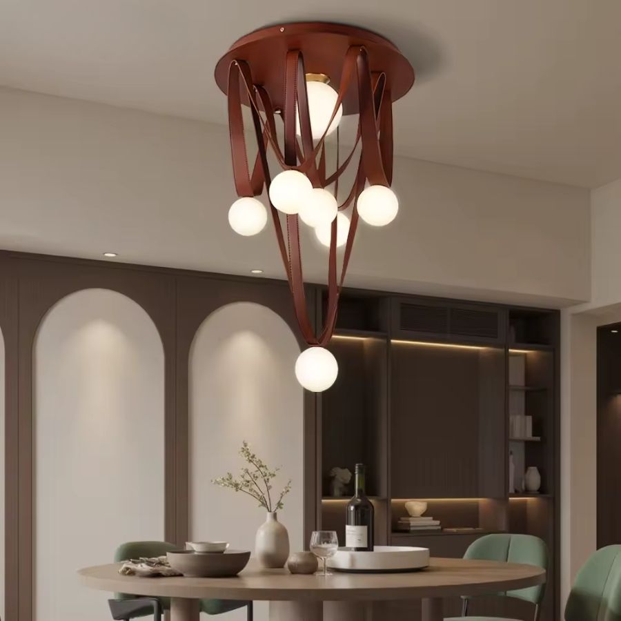 Au-dessus de la table, cette suspension sculpturale mêle lanières de cuir brun et globes en verre dépoli.