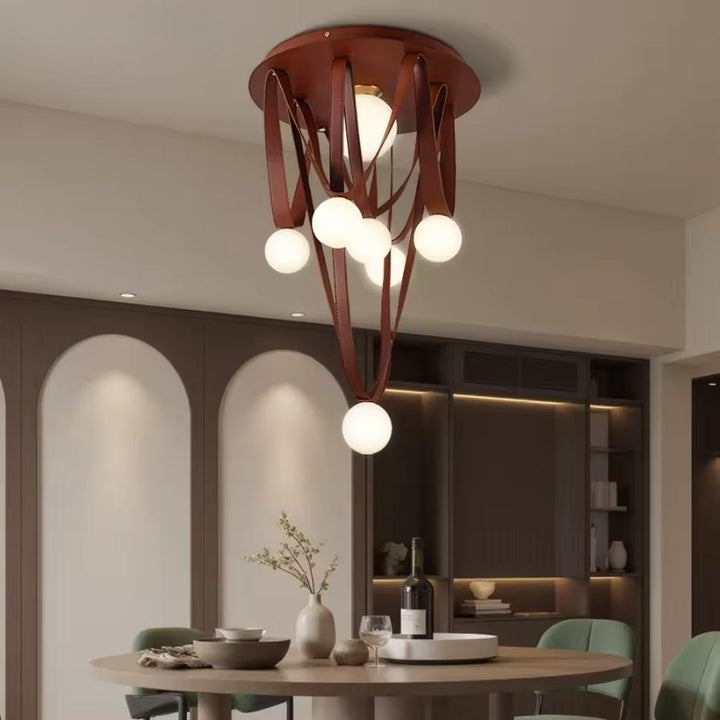 Au-dessus de la table, cette suspension sculpturale mêle lanières de cuir brun et globes en verre dépoli.