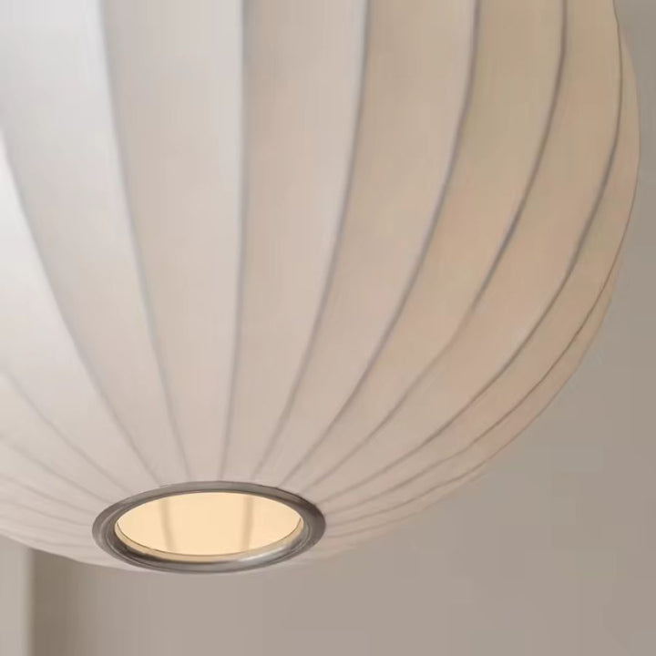 Gros plan sur l’abat-jour en soie blanche plissée d’une suspension globe au design organique, doux et contemporain