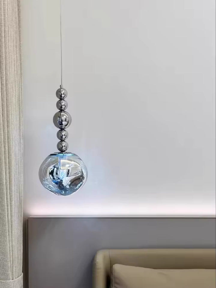 Près du lit, cette suspension à sphères chromées et globe transparent crée un accent design aux reflets délicats