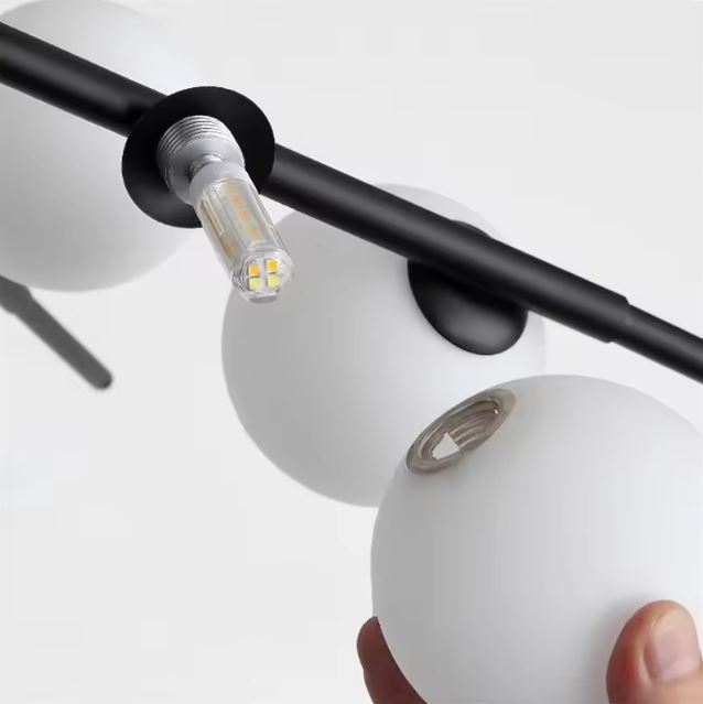 Installation d'une ampoule LED sur une suspension Sputnik avec globes en verre opale, un luminaire design et fonctionnel.