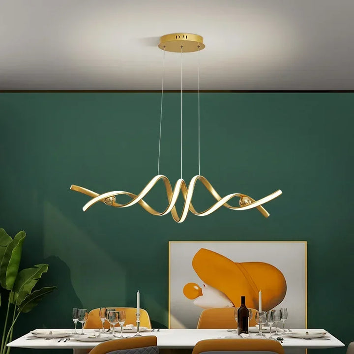 Suspension LED dorée aux lignes graphiques installée dans un espace repas chaleureux avec un mur vert émeraude.